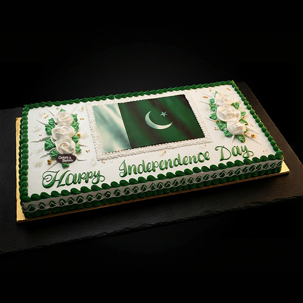 Pakistan Flag Celebration Cake with edible Pakistan national flag, Happy Independence Day green lettering, white frosting roses, green leaves, and piped green borders by Cakes and Bakes Bakery Duba